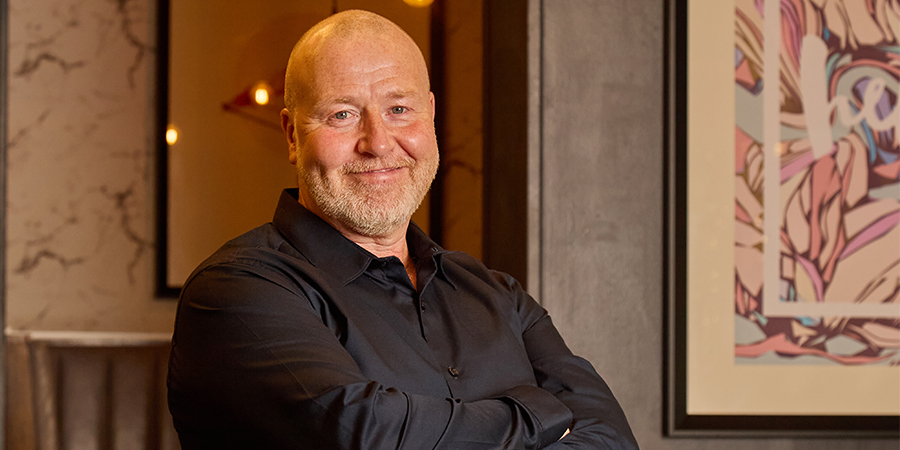 Male General Manager in a pub holding plates smiling towards the camera.