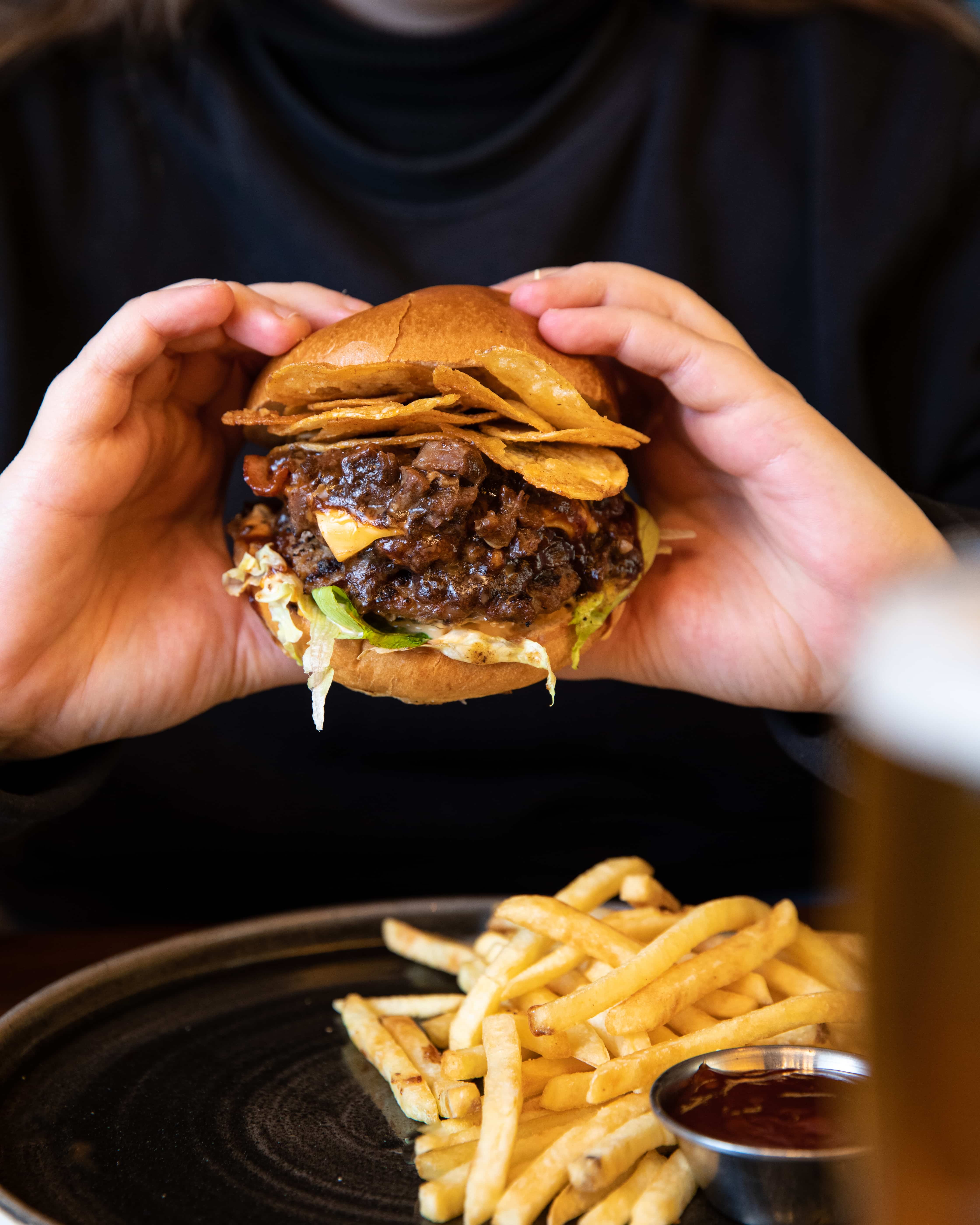 Beef and Ale burger being held with a side of fries