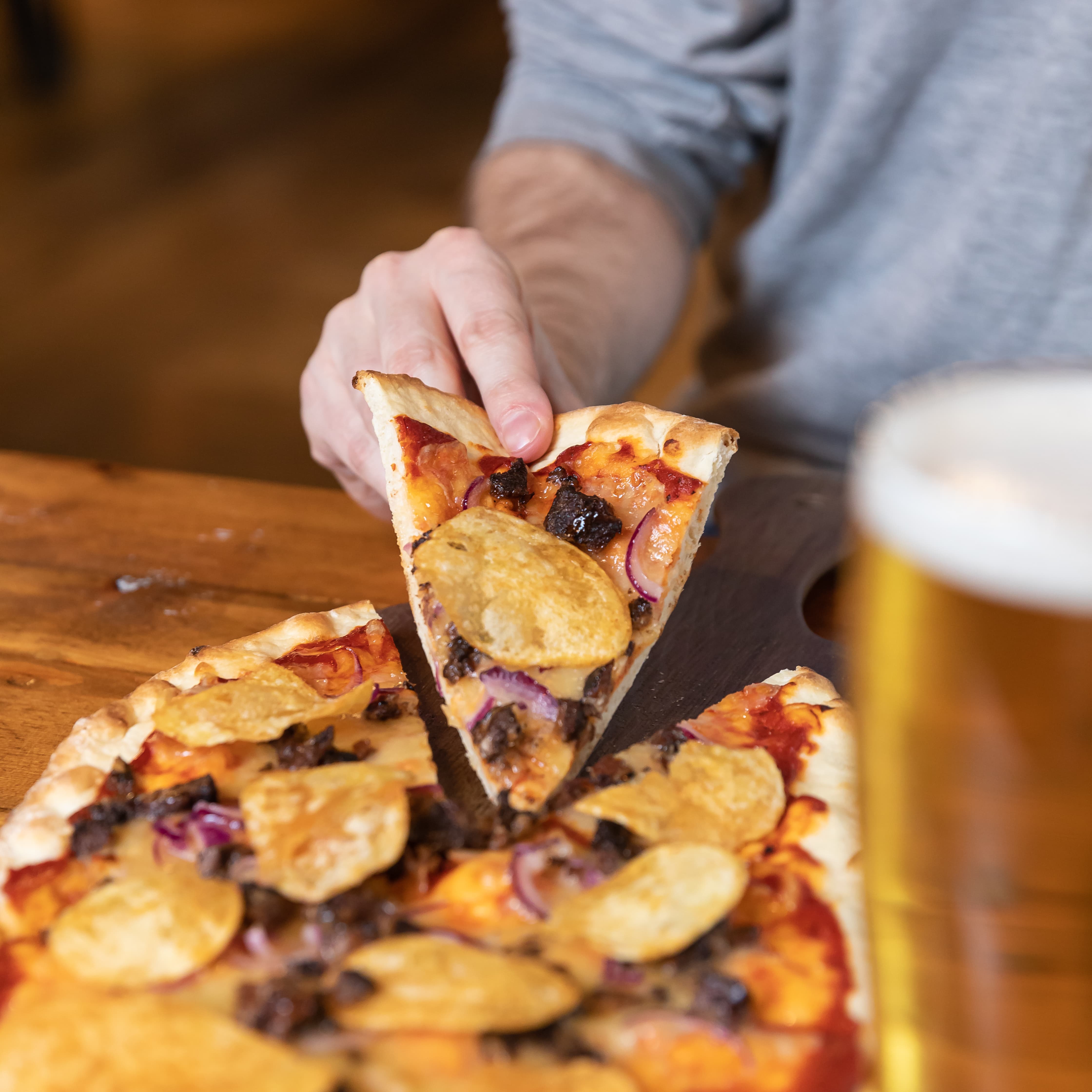 Hand holding a slice of a pizza with crisps on top