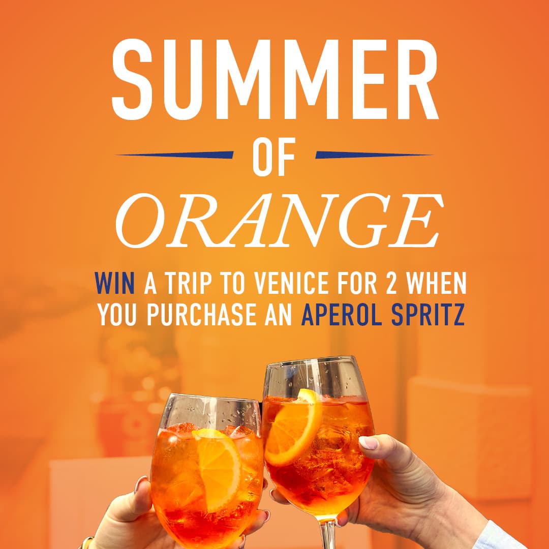 Two Aperol Spritz glasses next to a bottle of Aperol