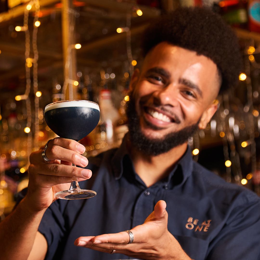 Be At One employee holding up a blue cocktail.
