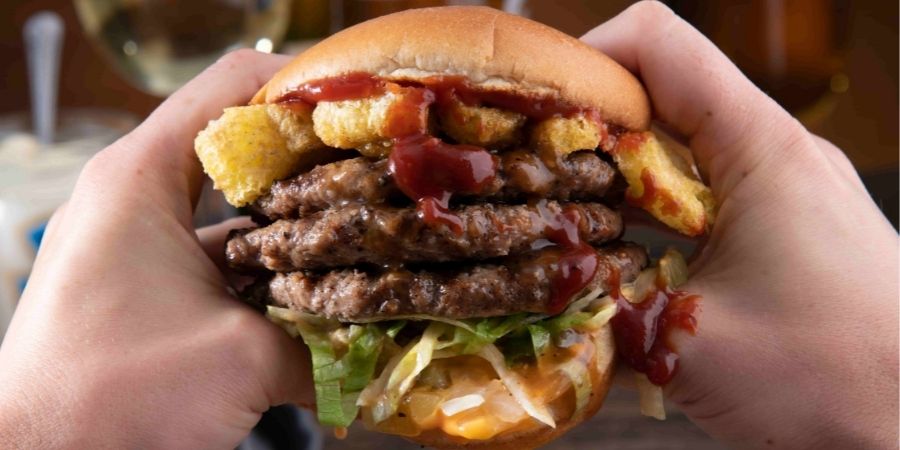 Burger with Multiple Patties and Cheese Held in Hands