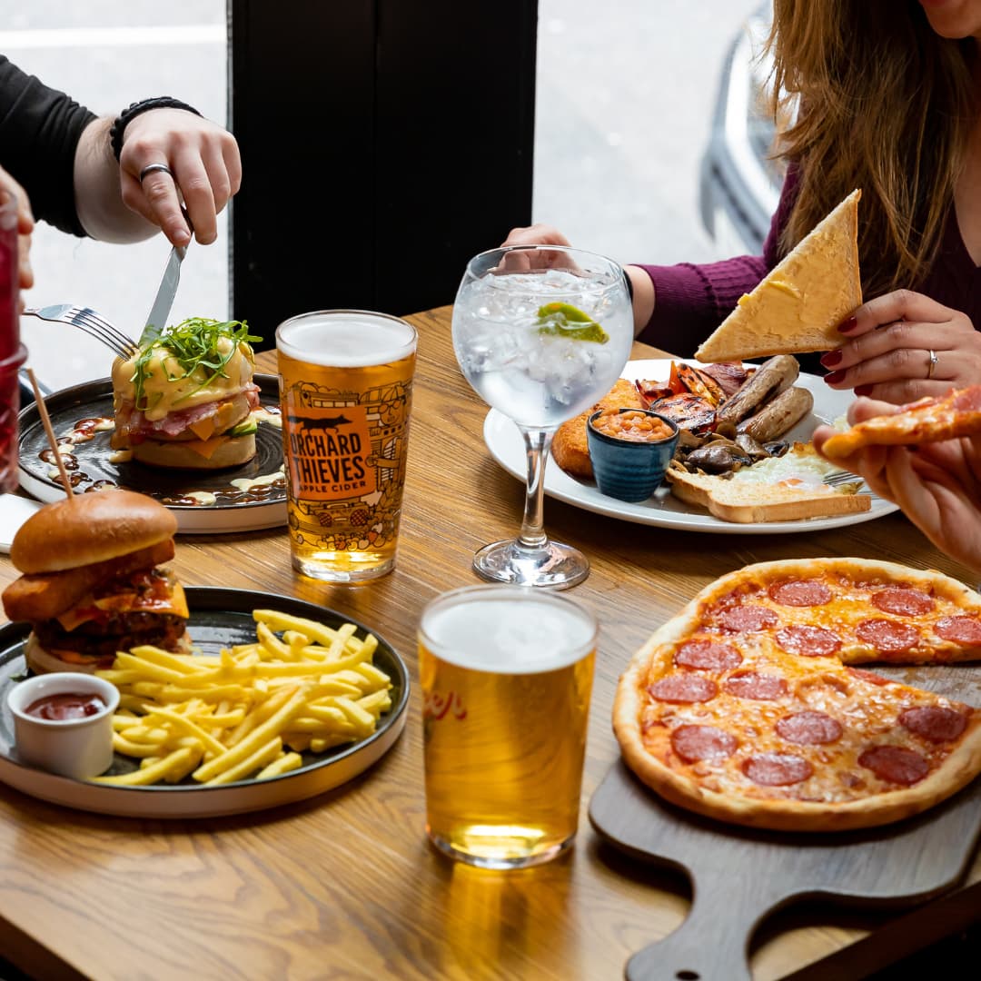 Stacked crumpets, burger and chips, pizza, and full English breakfast with beer, cider, and G&T