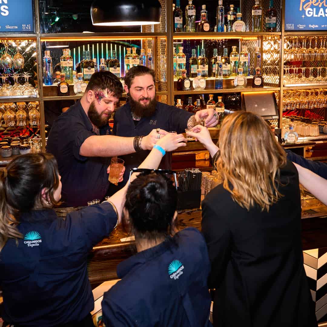 Contestants cheers'ing shots over the bar. 