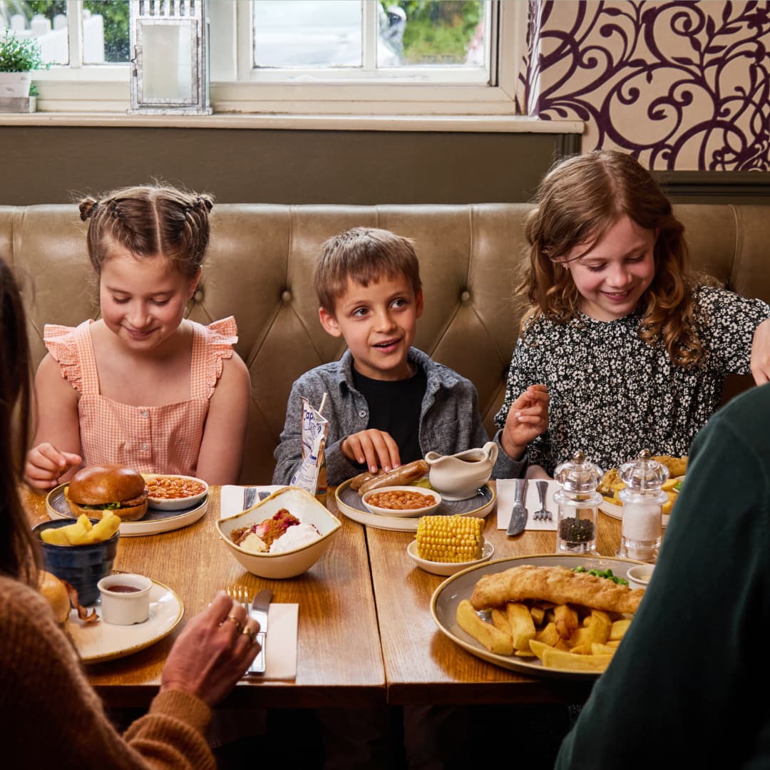 three children eating at a dining table in a pub