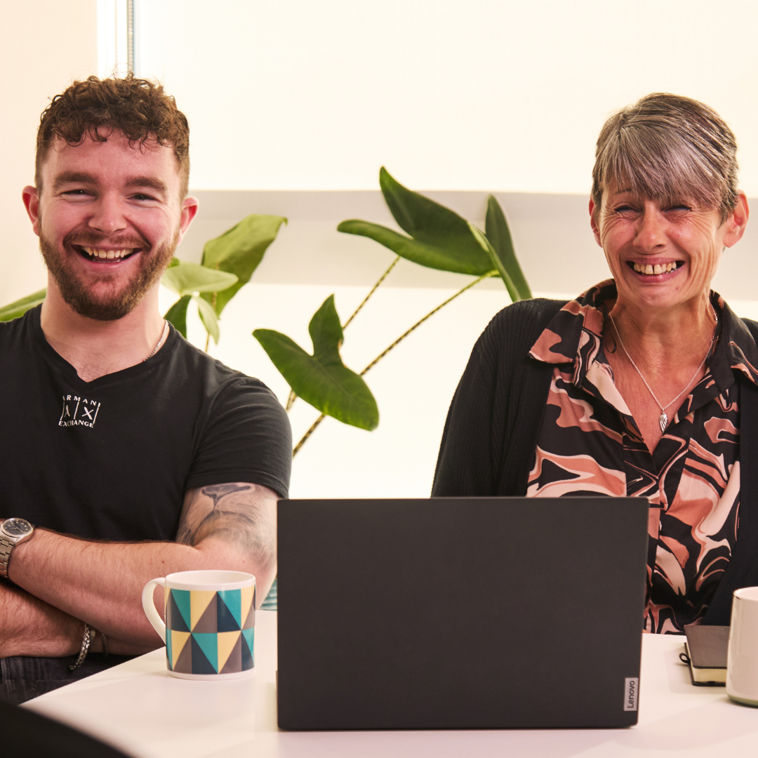 Two Finance team members smiling with a laptop in front.