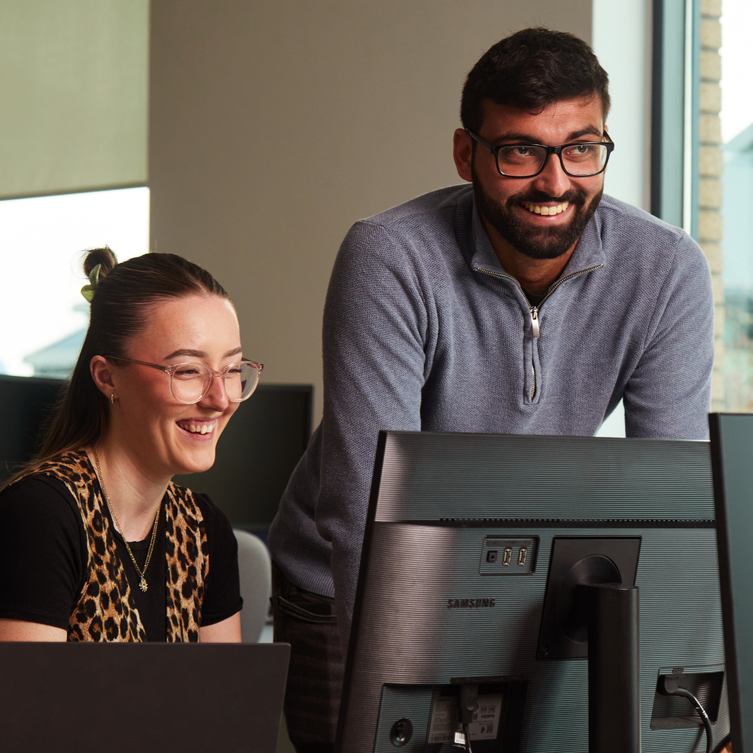 Two HR team members looking at a computer and smiling.