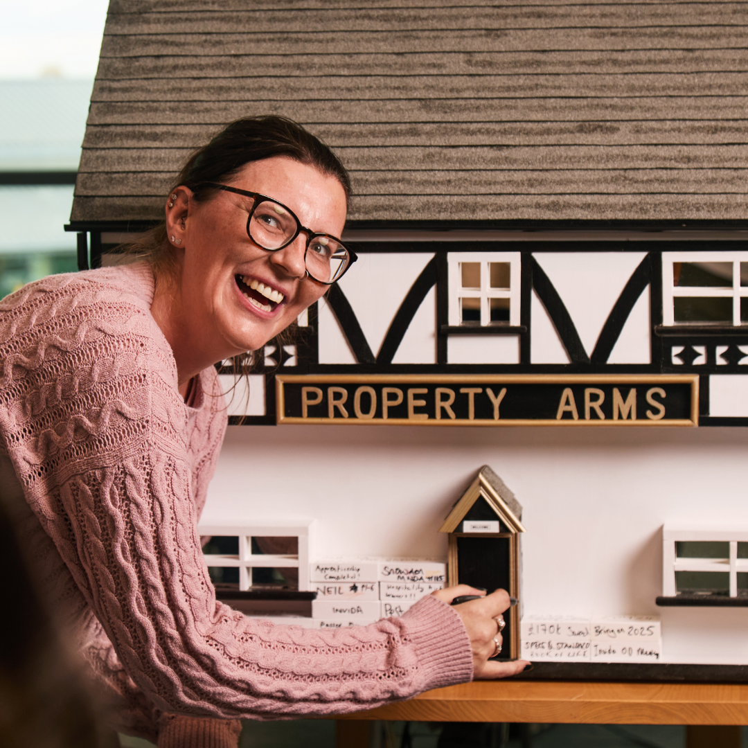 Property team member smiling in front of 'Property Arms' small house.