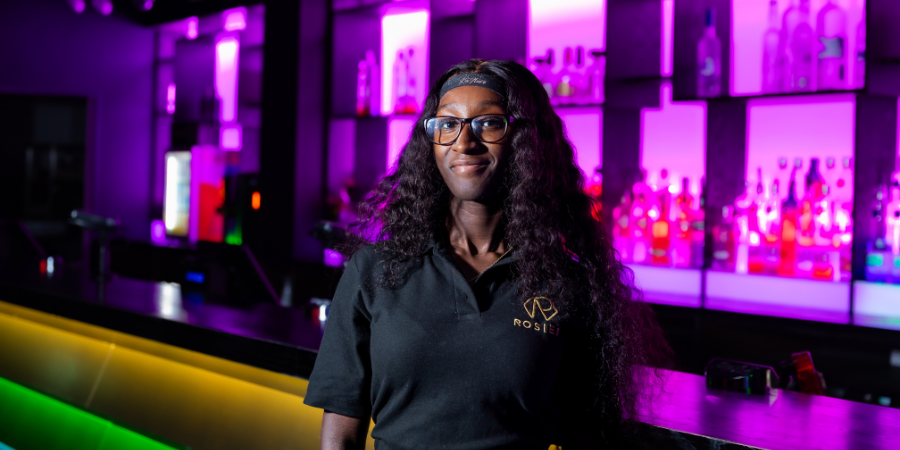 Bartender from Rosies leaning on the bar and smiling towards the camera.