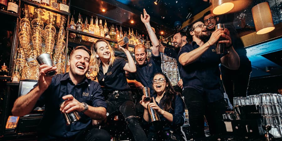 Seven Be At One bartenders perched on top of the bar posing for the camera.