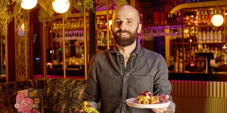 Waiter carrying plates to a table and smiling to the camera.