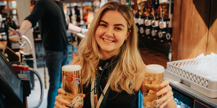 Deputy manager smiling towards the camera holding two pints.