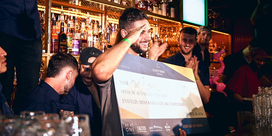 Jan holding a cheque behind the bar for winning Most Knowledgeable Bartender