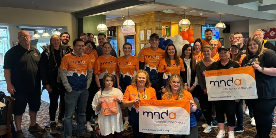 Image of teams posing in MNDA orange tops and holding the MNDA banner.